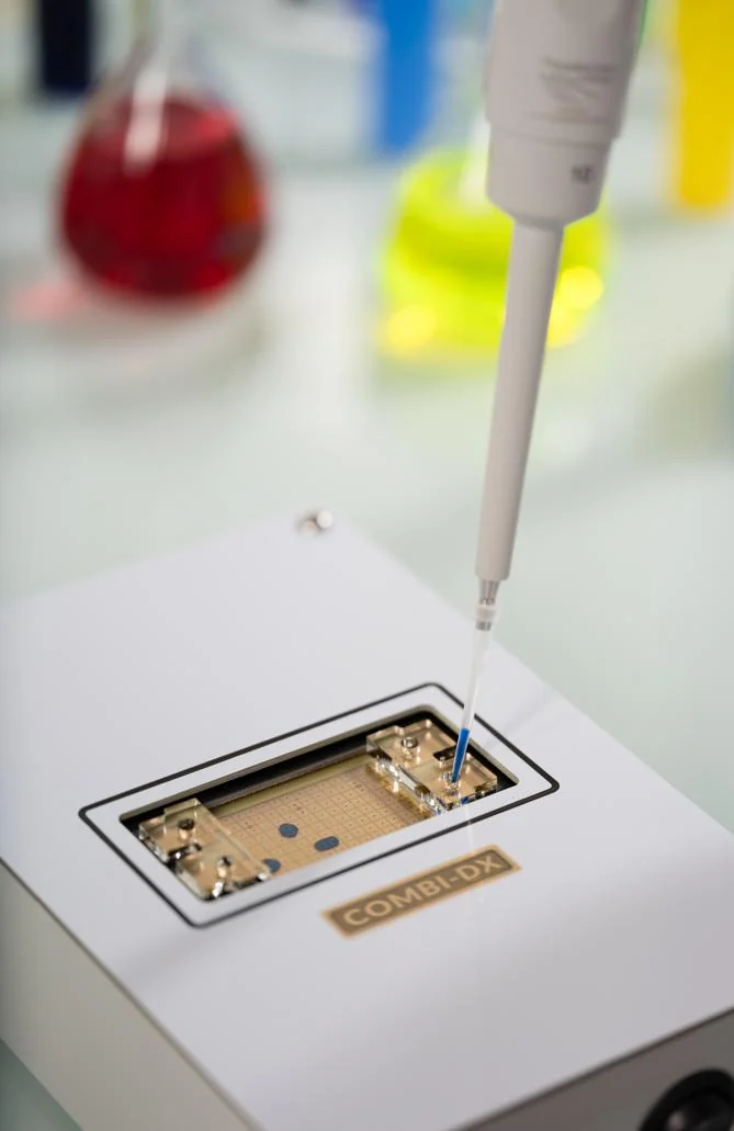 A pipette loads a sample into a digital microfluidic cartridge seated in its instrument, with droplets visible on the electrode array